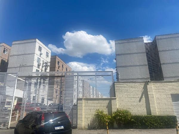Apartamento branco em condomínio com quatro blocos visíveis vista externa com portão e carro preto estacionado na frente