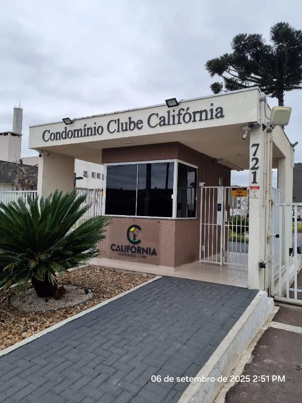 Apartamento no Condomínio Clube Califórnia com entrada do prédio branco e jardim bem cuidado na frente