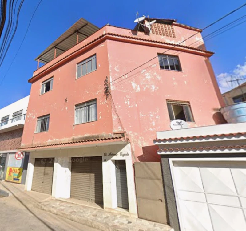Apartamento residencial rosa de 3 andares com janelas e portas metálicas em rua urbana fachada com pintura desgastada