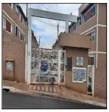 Apartamento bege em condomínio com portão branco e fachada de tijolos com entrada principal