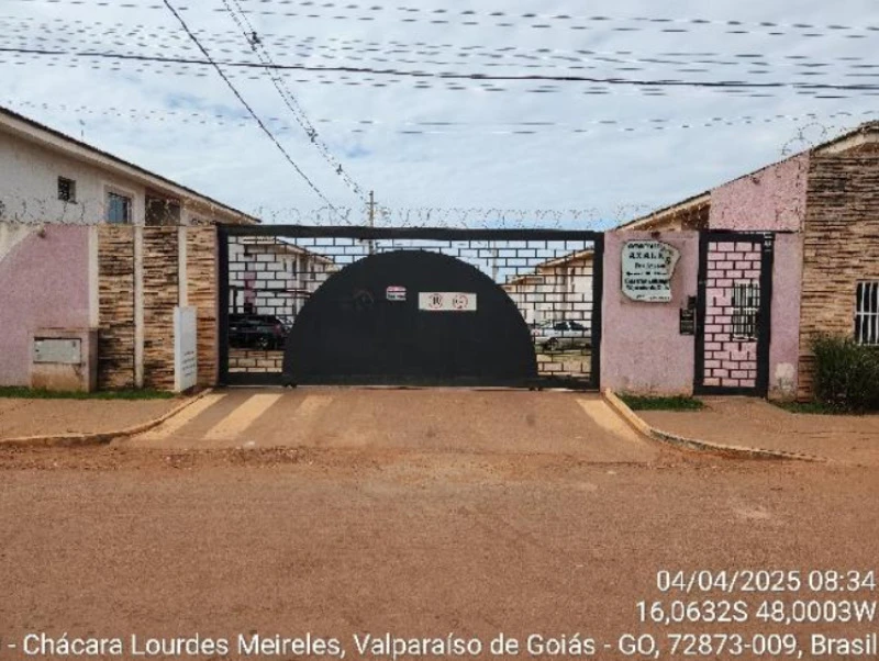 Apartamento bege em condomínio com portão preto e cerca elétrica, localizado em área residencial com casas semelhantes ao fundo