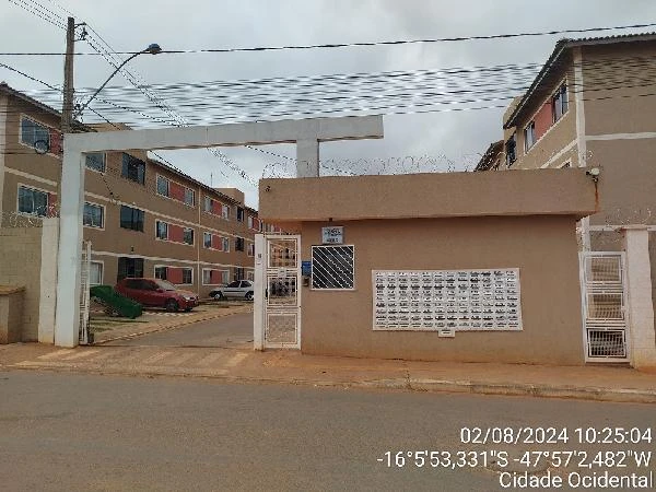 Apartamento em condomínio residencial com portaria e guarita, prédio de fachada bege, placas de correspondência visíveis e carros estacionados