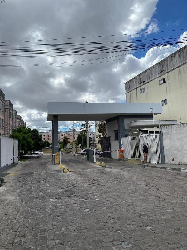 Apartamento branco com portaria em condomínio residencial, localizado em área urbana com pavimentação de paralelepípedo e cercado por prédios.