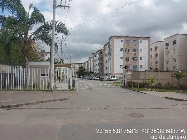 Apartamento em condomínio fechado com prédios claros de 4 andares, fachada simples, ruas asfaltadas e portaria com grades