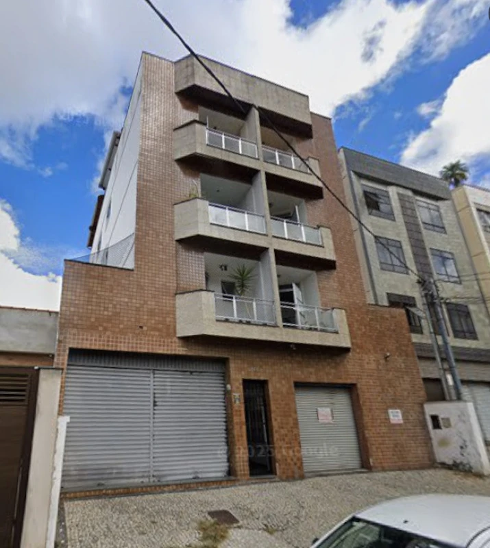 Apartamento com fachada de tijolos, sacadas com grades, duas portas de garagem metálica e entrada principal em área urbana