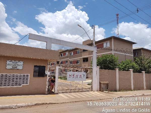 Apartamento em condomínio residencial com fachada em tom bege, portão branco e cerca de muro baixo