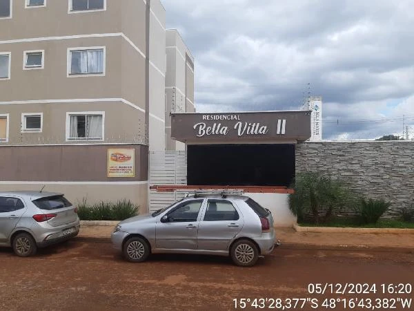 Apartamento bege no Condomínio Residencial Bella Vitta II com fachada visível e carros estacionados em rua de terra