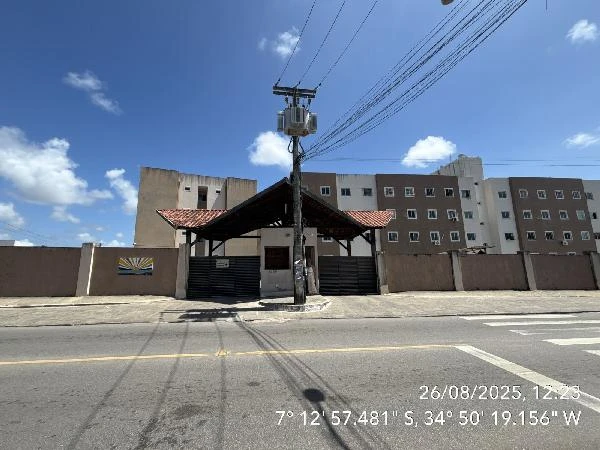 Apartamento branco em condomínio residencial com portaria coberta e prédio de fachada simples em área urbana