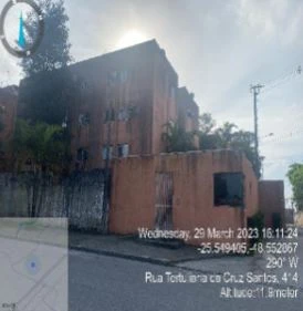 Apartamento em prédio de fachada desgastada em rua residencial com muro e vegetação próxima