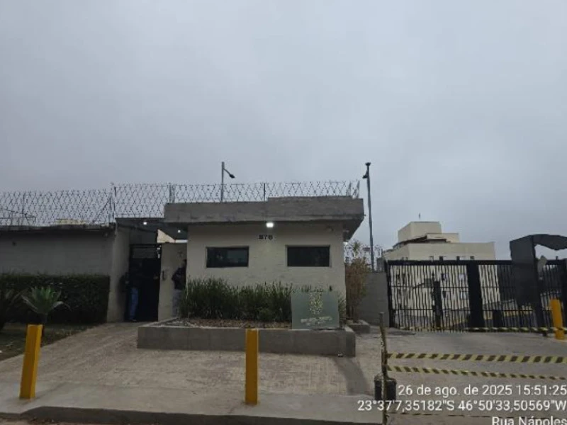 Apartamento localizado em condomínio residencial com fachada simples, guarita com cerca e portão de ferro no entorno