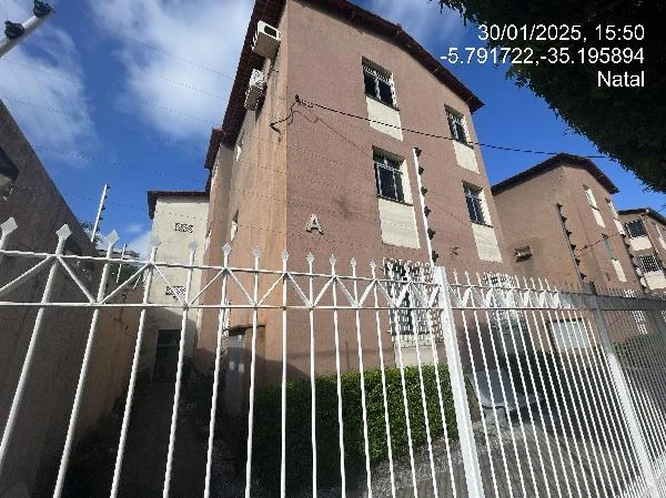 Apartamento bege em condomínio residencial com grades metálicas no entorno e ambiente externo com céu claro