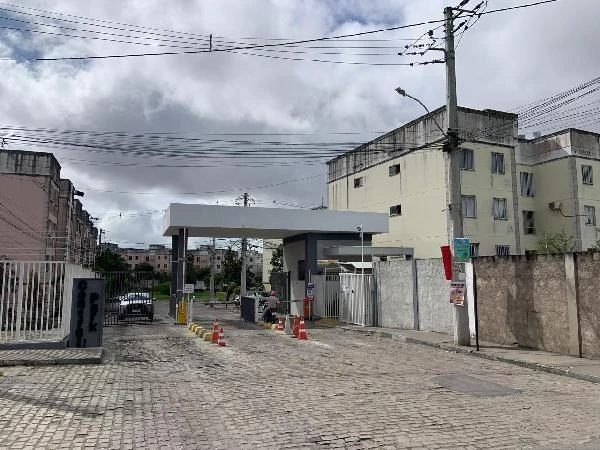Apartamento em condomínio residencial com guarita de entrada, prédio de fachada clara e ambiente pavimentado