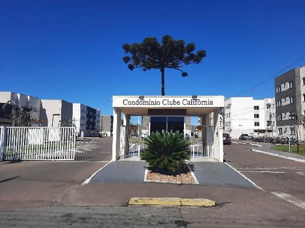 Apartamento no Condomínio Clube Califórnia com entrada principal e prédios residenciais visíveis ao fundo em área urbana