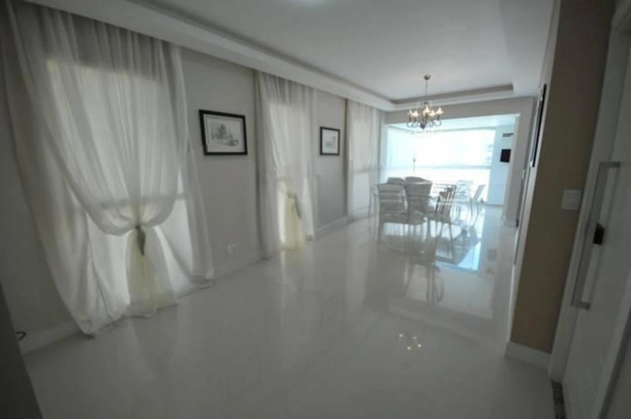 Apartamento branco com sala de jantar mobiliada, piso brilhante e janela ampla com cortinas brancas em área interna