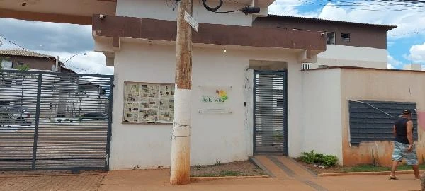 Apartamento branco em condomínio com portão metálico e placa Bella Vita na entrada e homem ao lado