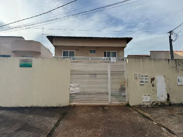 Apartamento em condomínio com fachada bege, portão branco e garagem visível na frente, imóvel com paredes externas sem avarias aparentes