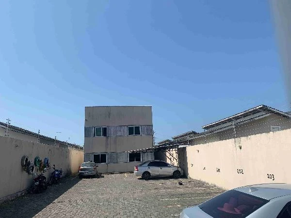 Apartamento com fachada simples e garagem descoberta com carros estacionados em pavimento de paralelepípedo sob céu claro