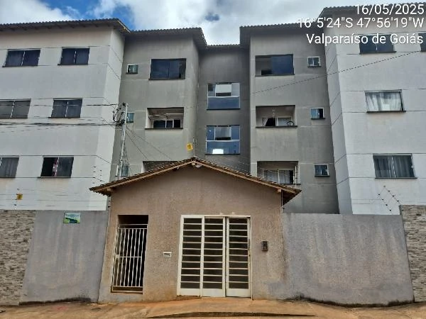 Apartamento de fachada cinza claro em condomínio residencial com portão branco e muro de concreto