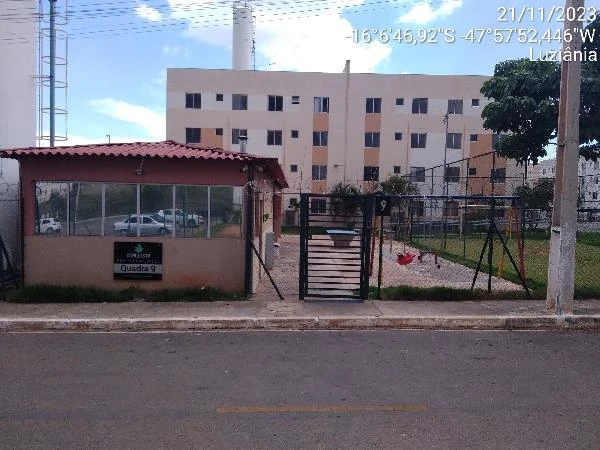 Apartamento residencial bege com portão preto, área de lazer com playground e quadra cercada em condomínio em Luziania