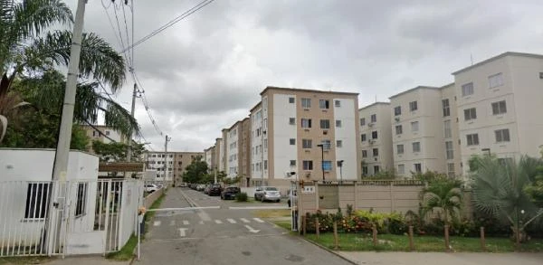 Apartamento branco em condomínio residencial com quatro andares, área externa com entrada e carros estacionados na rua, céu nublado