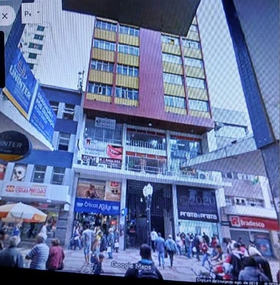 Apartamento com fachada comercial em rua movimentada no centro, vários comércios no térreo e pessoas na calçada