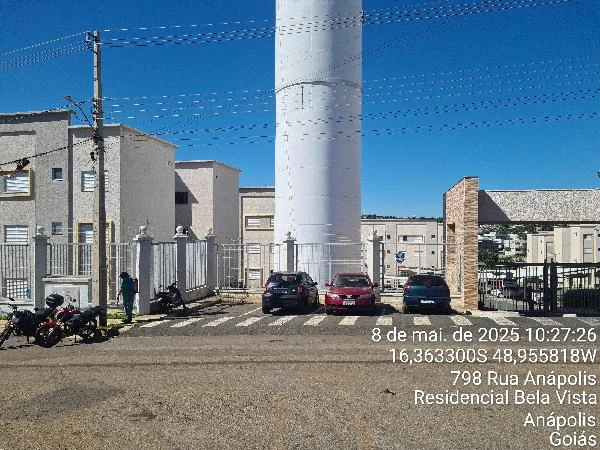 Apartamento em condomínio com fachada clara, portão de entrada, vagas externas e torre de reservatório ao fundo