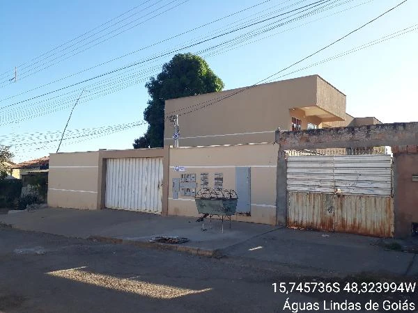 Apartamento bege em condomínio residencial com garagem e portões brancos em rua asfaltada com sombra de árvore