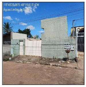 Apartamento em condomínio com fachada cinza clara, portão branco e rua de terra em frente