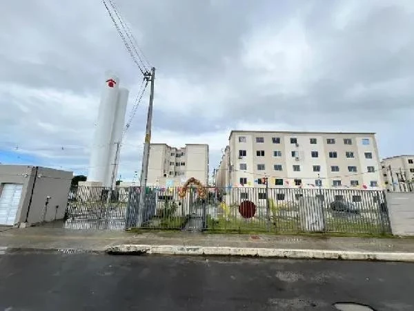 Apartamento branco de 41m² em condomínio fechado com cerca metálica ao redor sob céu nublado