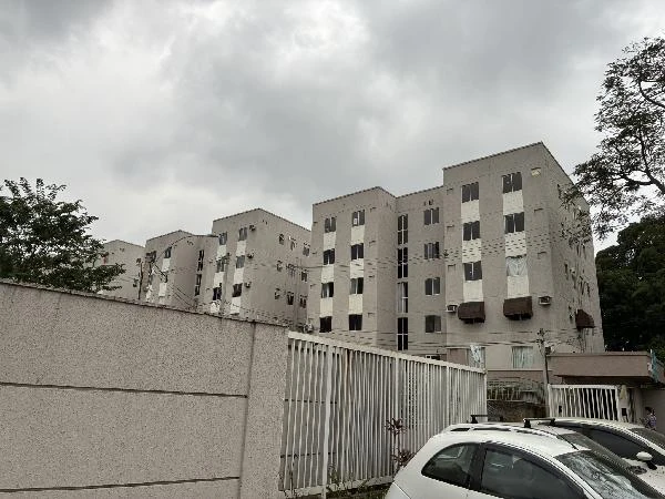 Apartamento cinza em condomínio residencial com cinco andares e portão branco em dia nublado carros estacionados