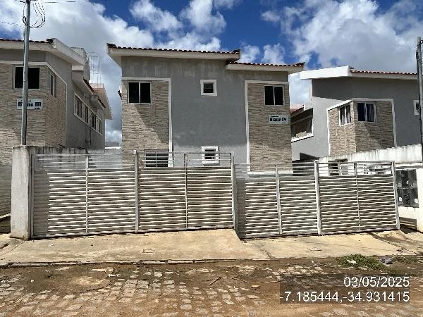 Apartamento cinza claro e bege em condomínio com portão metálico e duas vagas, fachada com acabamento moderno e céu azul ao fundo