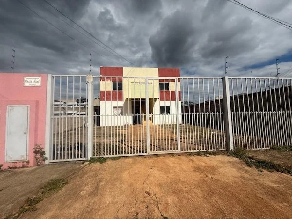 Apartamento de dois andares com fachada branca e detalhes vermelhos, com portão metálico e área externa descoberta