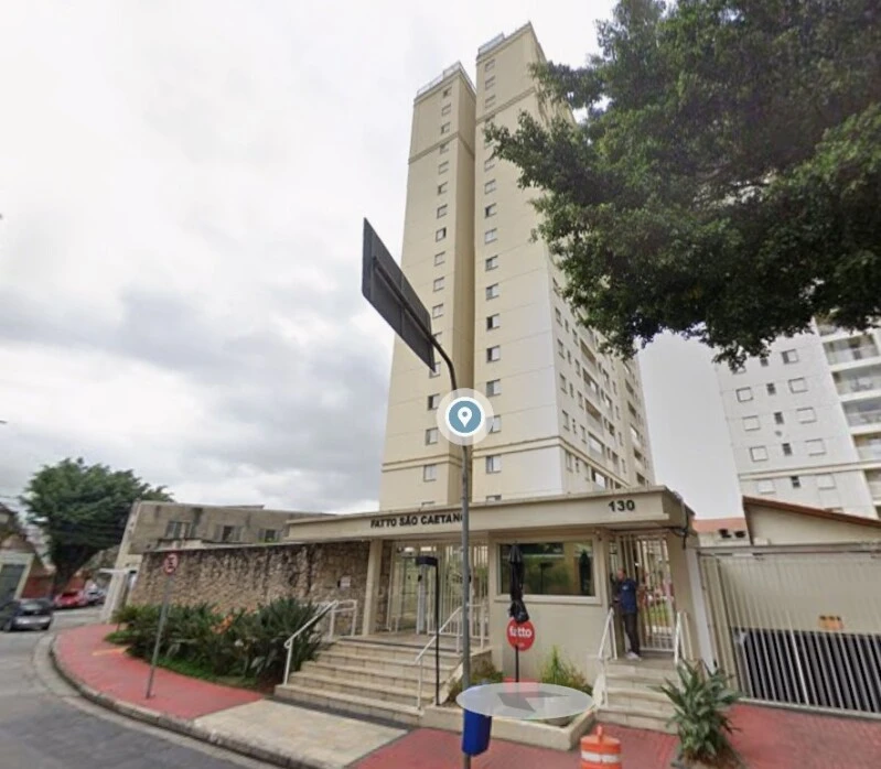 Apartamento branco em condomínio residencial com entrada principal e área ajardinada na rua