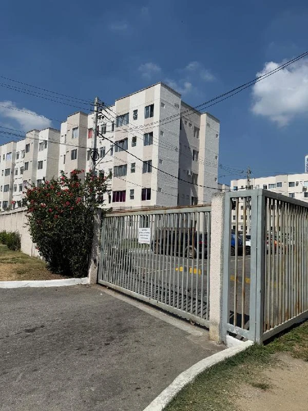 Apartamento branco em condomínio fechado com portão metálico e área externa pavimentada sob céu azul