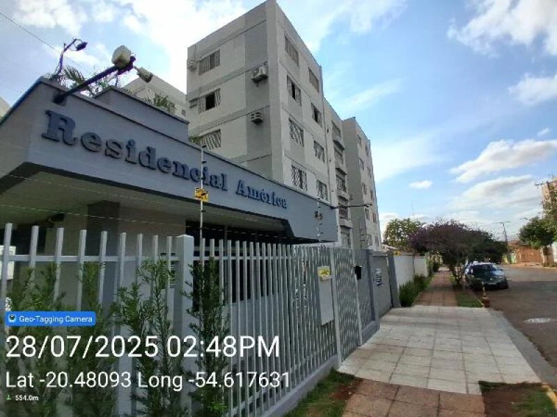 Apartamento branco no Condomínio Residencial América com grades de segurança e calçada ao redor em dia aberto