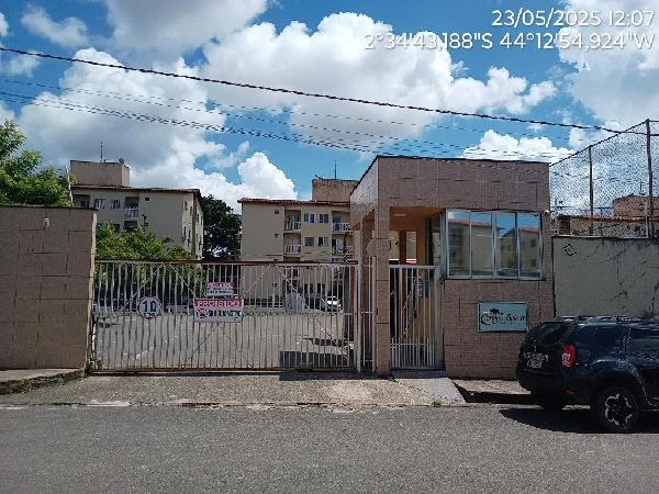 Apartamento com fachada de condomínio residencial, portão de ferro, guarita na entrada e veículo estacionado na rua em frente