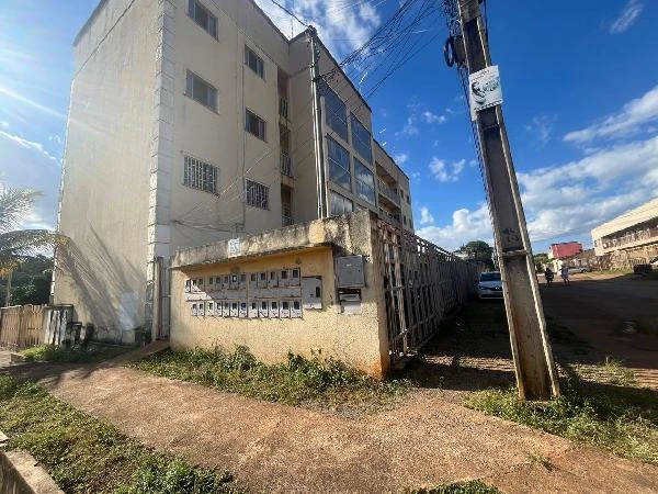 Apartamento branco em condomínio residencial com quatro andares fachada levemente desgastada e cerca metálica