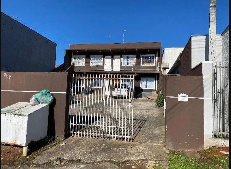 Apartamento bege em condomínio com 2 andares, portão branco de metal e vaga com carro estacionado