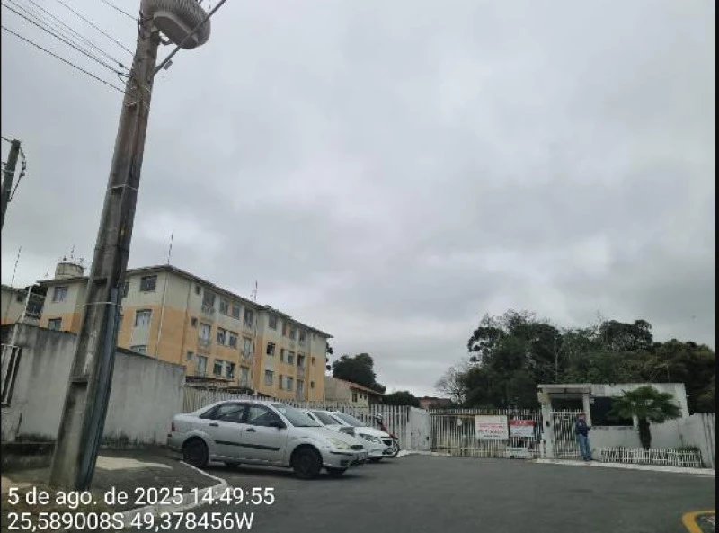 Apartamento cinza em condomínio residencial com 1 vaga de garagem e bloco de prédios ao fundo sob céu nublado