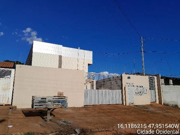 Apartamento branco com varanda em condomínio residencial, fachada simples com portão metálico em área urbana