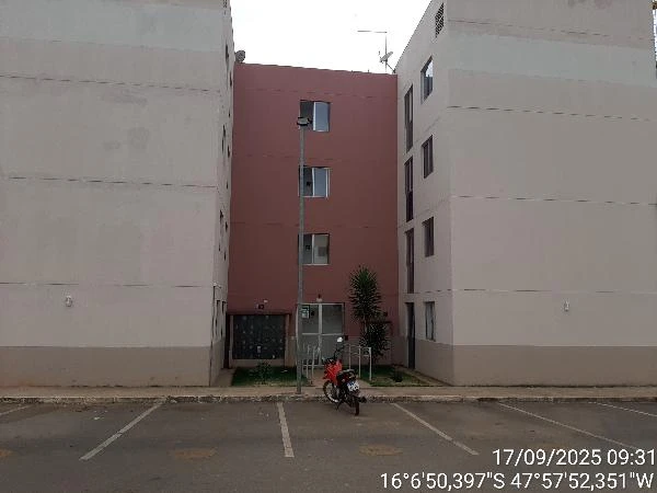 Apartamento com fachada clara e entrada central entre dois blocos em condomínio residencial com estacionamento em frente