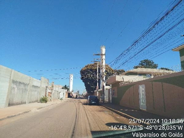 Apartamento com fachada verde em rua asfaltada com postes e carros estacionados sob céu claro em Valparaíso de Goiás