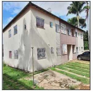 Apartamento bege em condomínio residencial com 2 andares, janelas com grades e gramado frontal, sem avarias visíveis