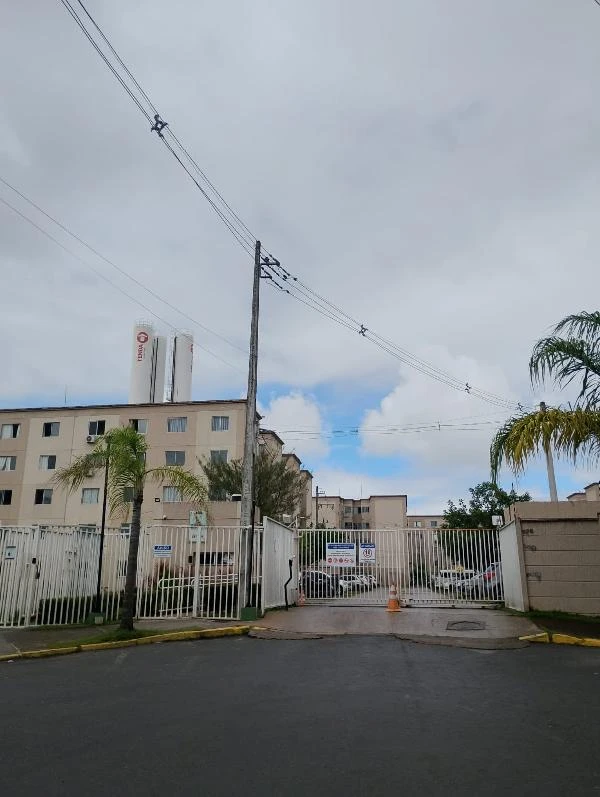 Apartamento no condomínio com fachada clara, grades brancas, área externa com palmeiras e céu nublado