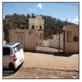 Apartamento bege em condomínio fechado com portão metálico e carro branco estacionado na frente em área residencial