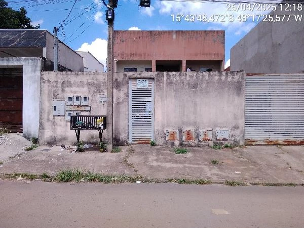 Apartamento com fachada simples, muro com portão de metal e paredes manchadas em área urbana