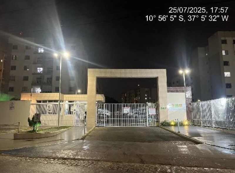 Apartamento em condomínio fechado com portaria iluminada à noite e prédios residenciais ao fundo sem avarias visíveis