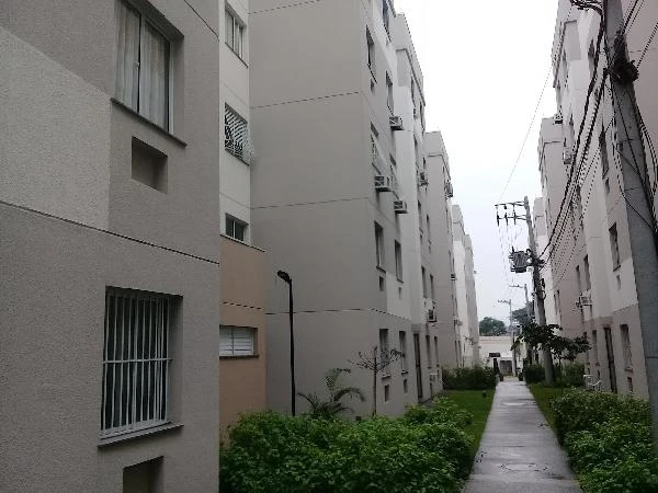 Apartamento branco em condomínio residencial com 5 andares, área comum com calçada e vegetação bem cuidada em dia nublado