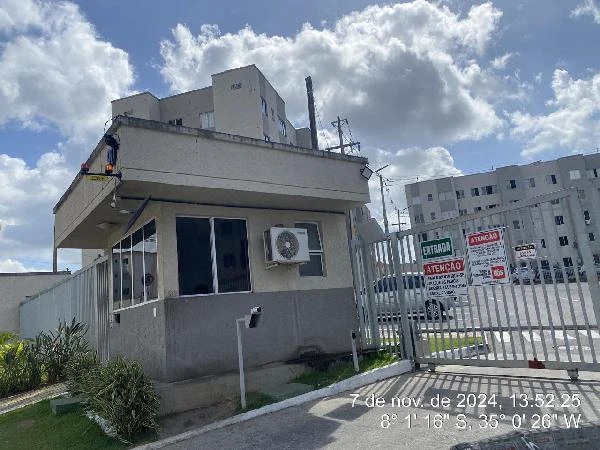 Apartamento na cor bege com ar-condicionado na fachada e portaria com guarita em condomínio residencial durante o dia ensolarado