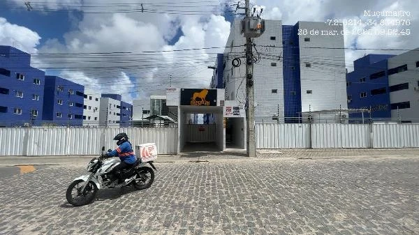 Apartamento branco em condomínio residencial com fachada moderna e portaria central envolta por muro